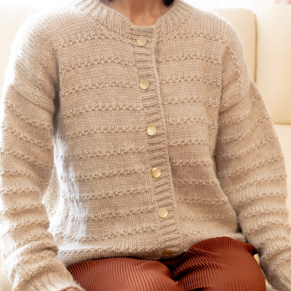 A woman sitting wearing a cardigan made of natural alpaca yarn.